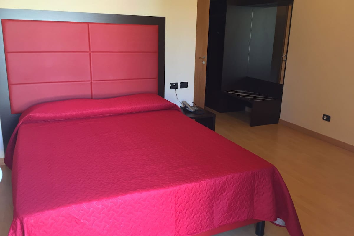 Una habitación de hotel con una cama grande, un armario de madera y una mesita de noche con teléfono.