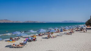 A beach with rows of blue and white striped umbrellas and lounge chairs. - Cavo D'oro Hotel (Kos)