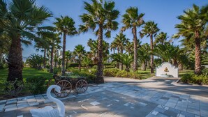 A paved pathway with a swan sculpture, palm trees, and a carriage in a landscaped area. - Cavo D'oro Hotel (Kos)