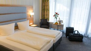 A hotel room with a large bed, a chair, a small table with a vase of flowers, and a suitcase. - Seehotel Forst (Forst)