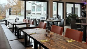 A modern restaurant with large windows, wooden tables, and leather seating. - Seehotel Forst (Forst)