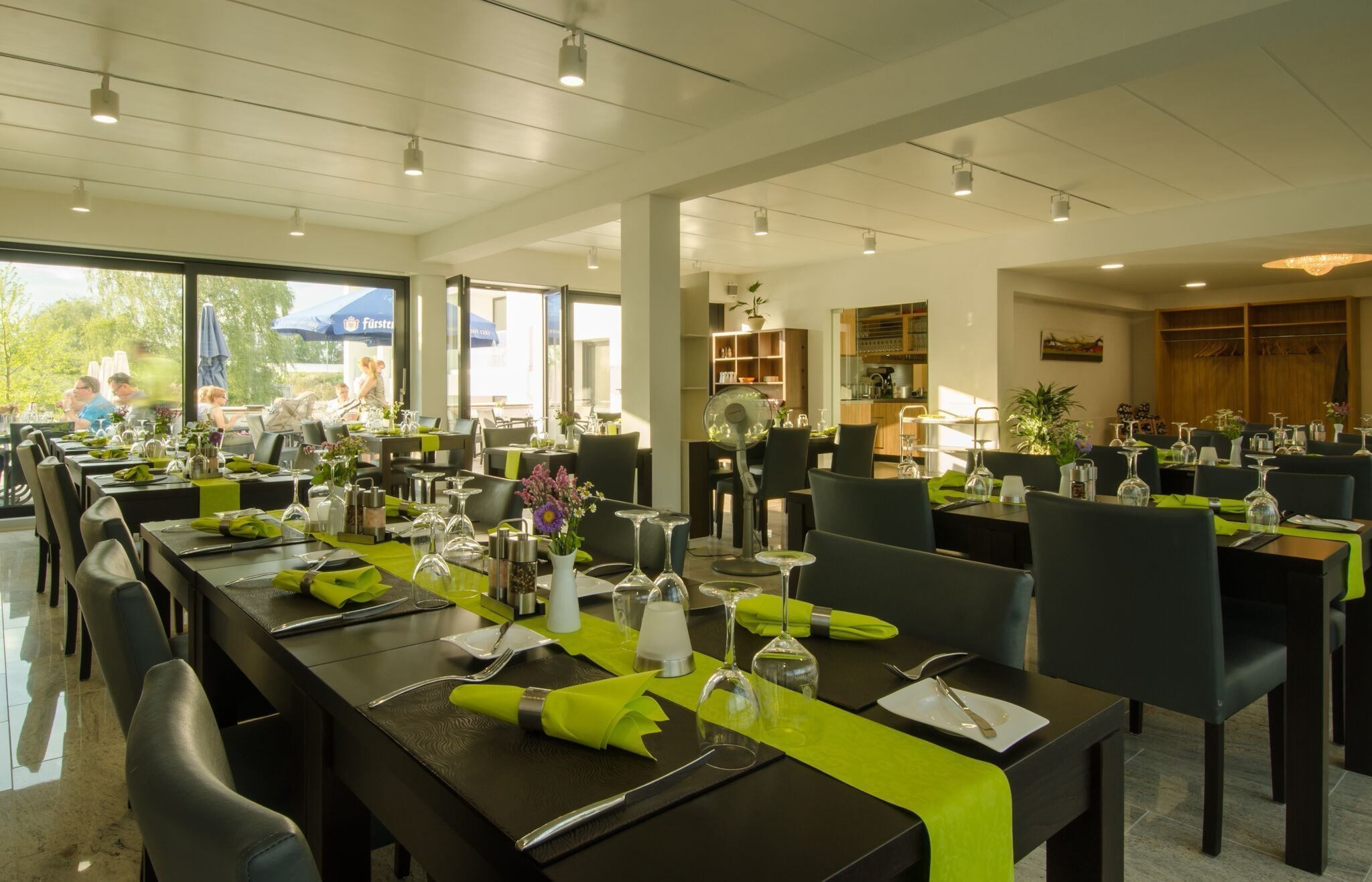 A restaurant with multiple dining tables, each set with green napkins, cutlery, and glassware.