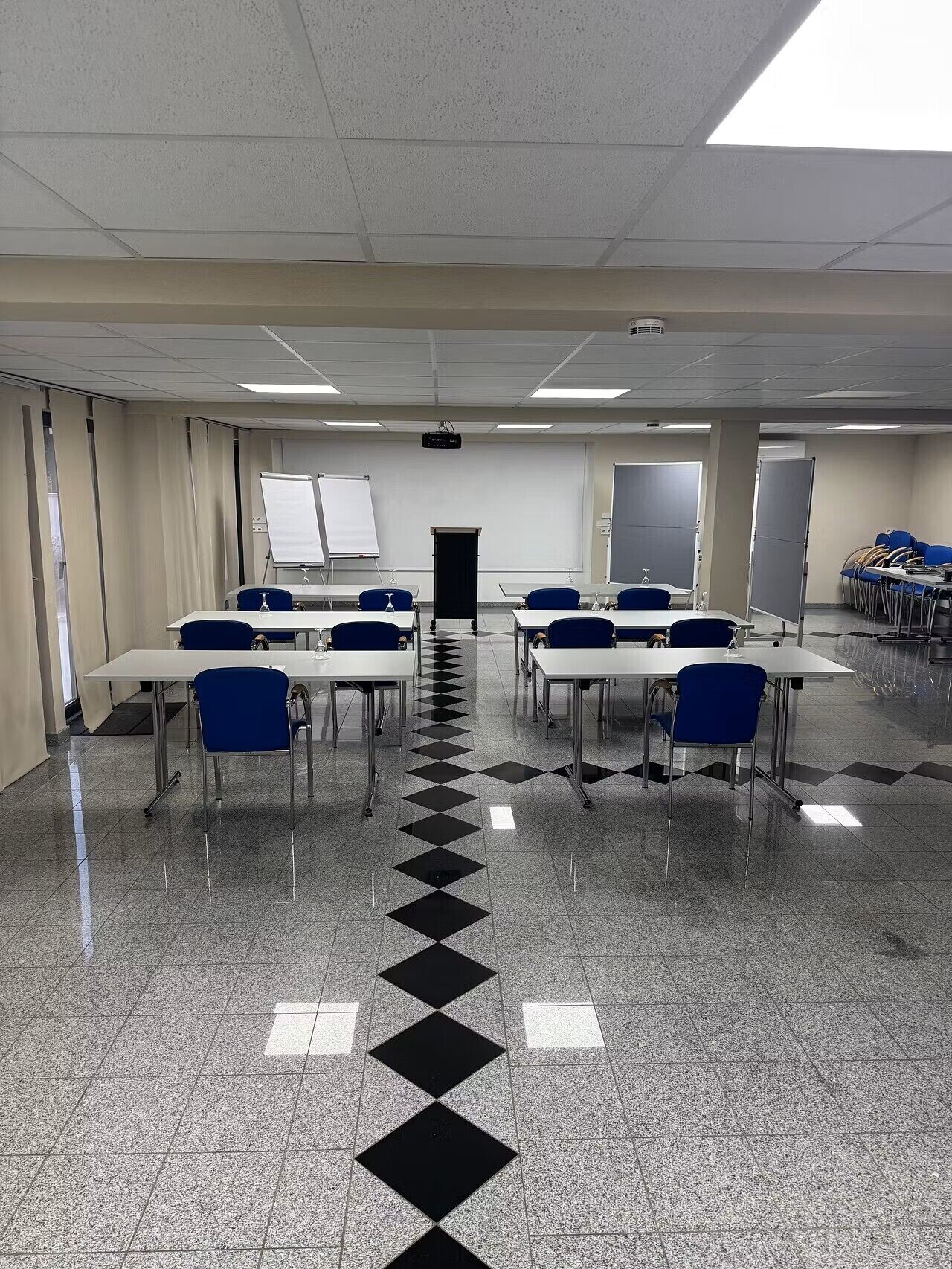 A conference room with a checkered floor, white tables, blue chairs, a projector, and a whiteboard.