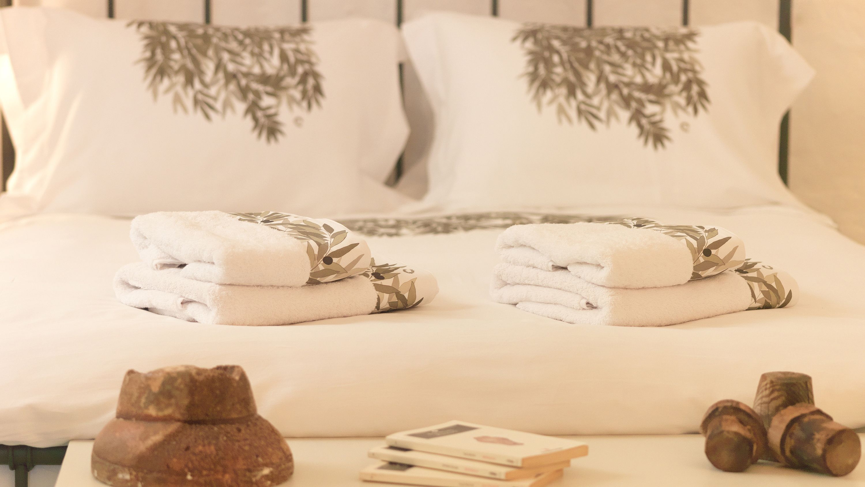 A neatly made bed with folded towels, a wooden sculpture, and a stack of books.