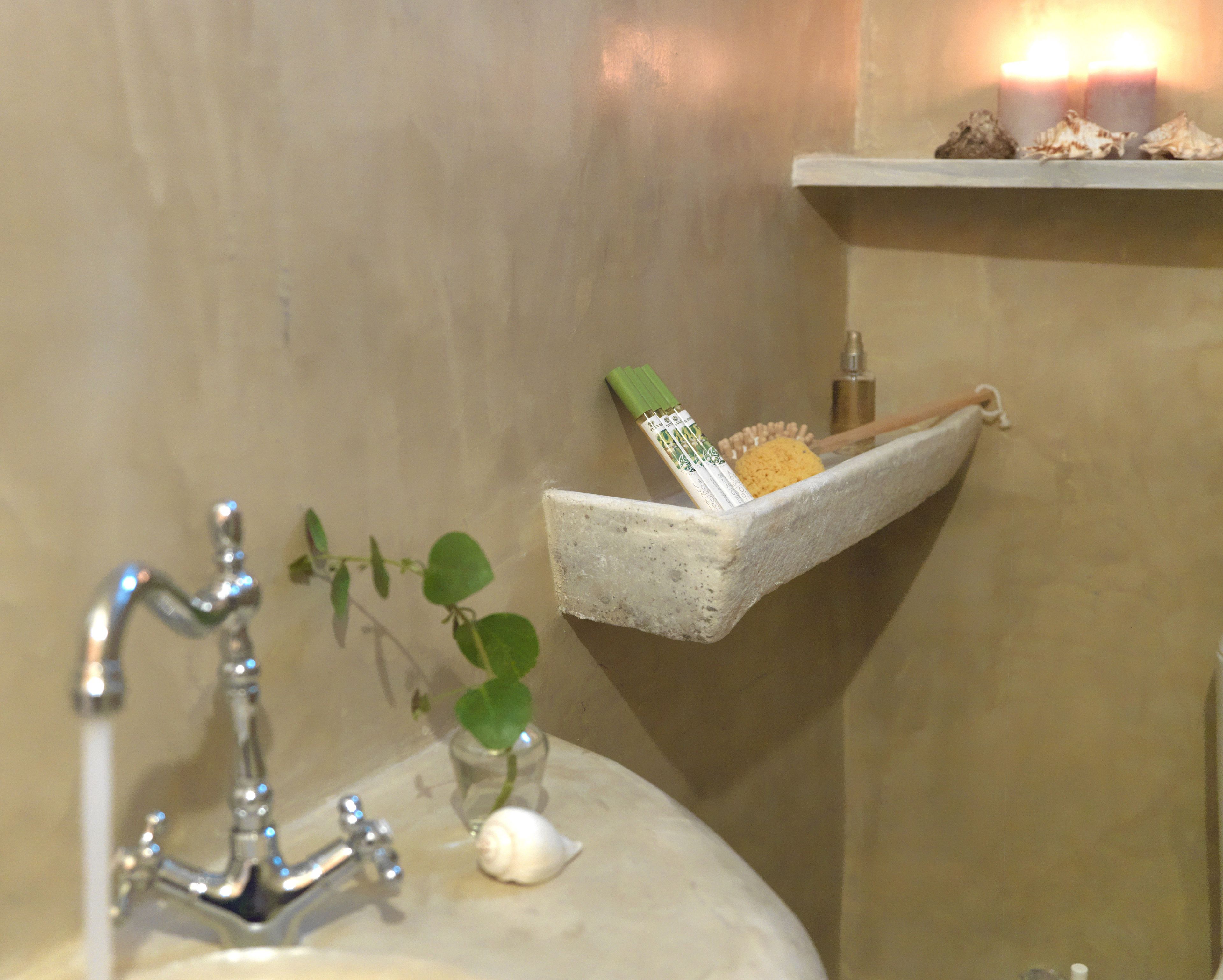 Een badkamer met een wastafel, een kraan, een klein plantje, een slak en een plankje met een tandenborstel en schelpen.