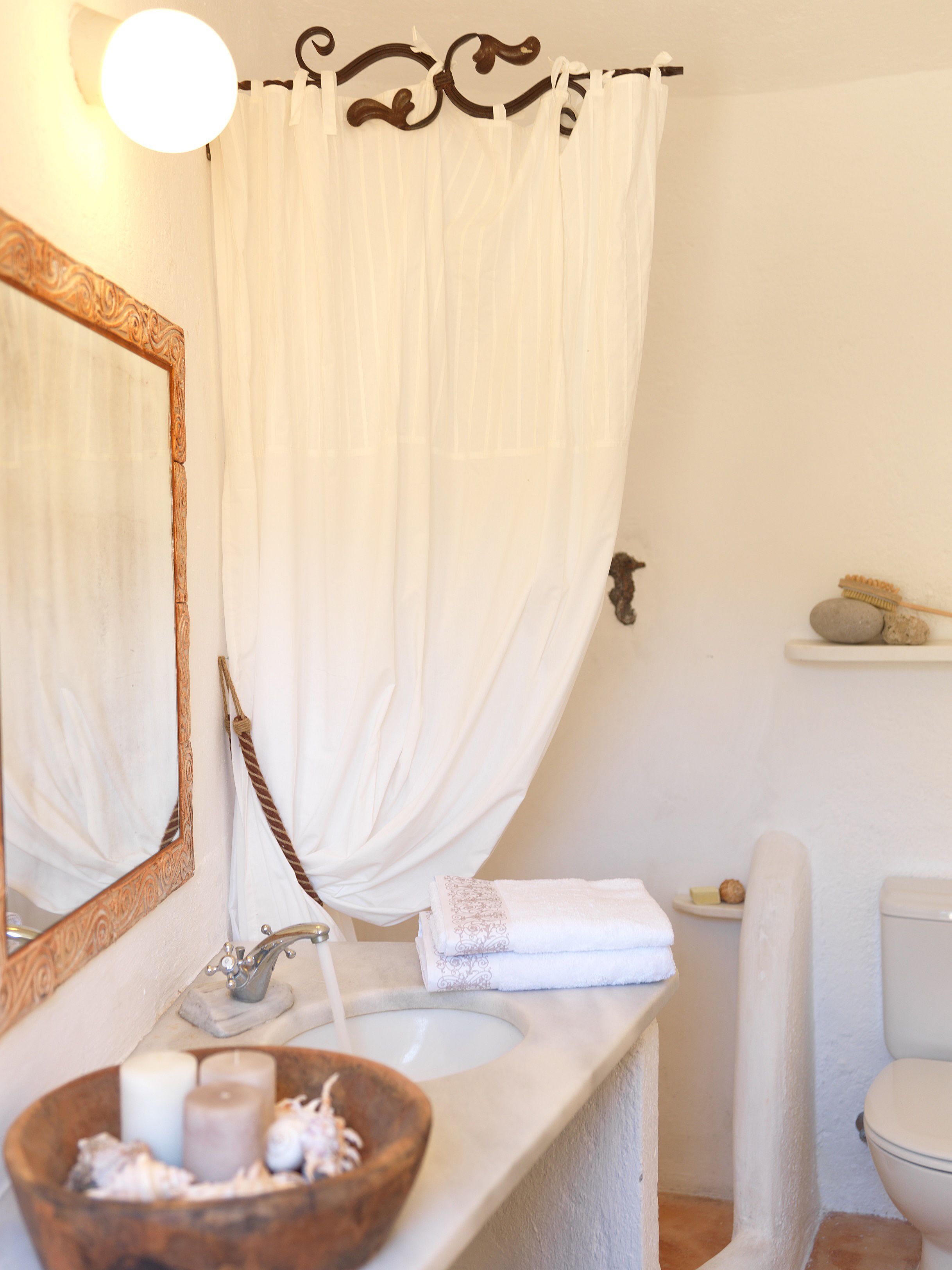 Un bagno con uno specchio con cornice in legno, un lavandino bianco, una vasca da bagno bianca con tenda e un water.