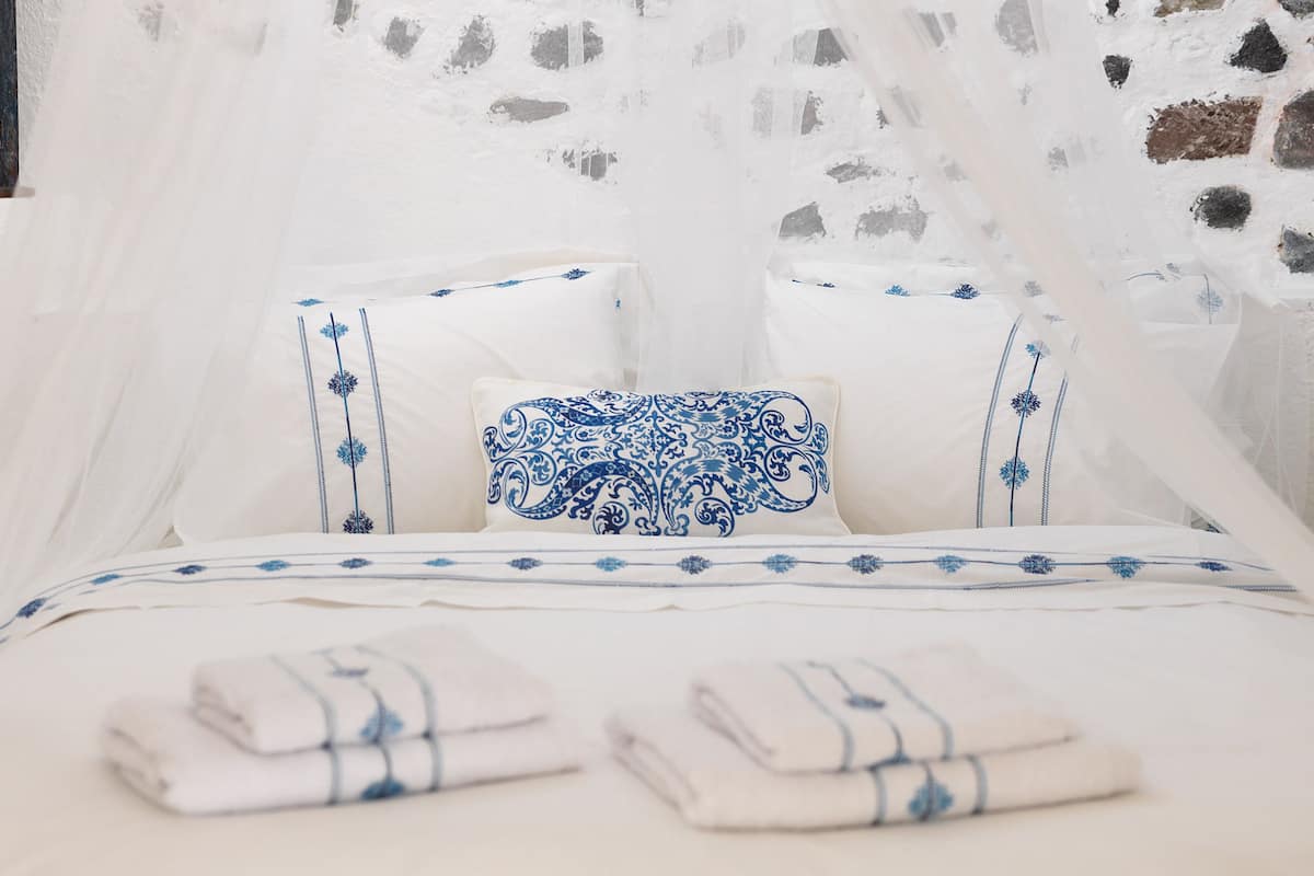 A bed with white bedding and blue floral patterns, a white canopy, and a stone wall.