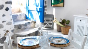 Una mesa dispuesta con platos, vasos y una jarrón, con una escalera y una cesta de flores al fondo.