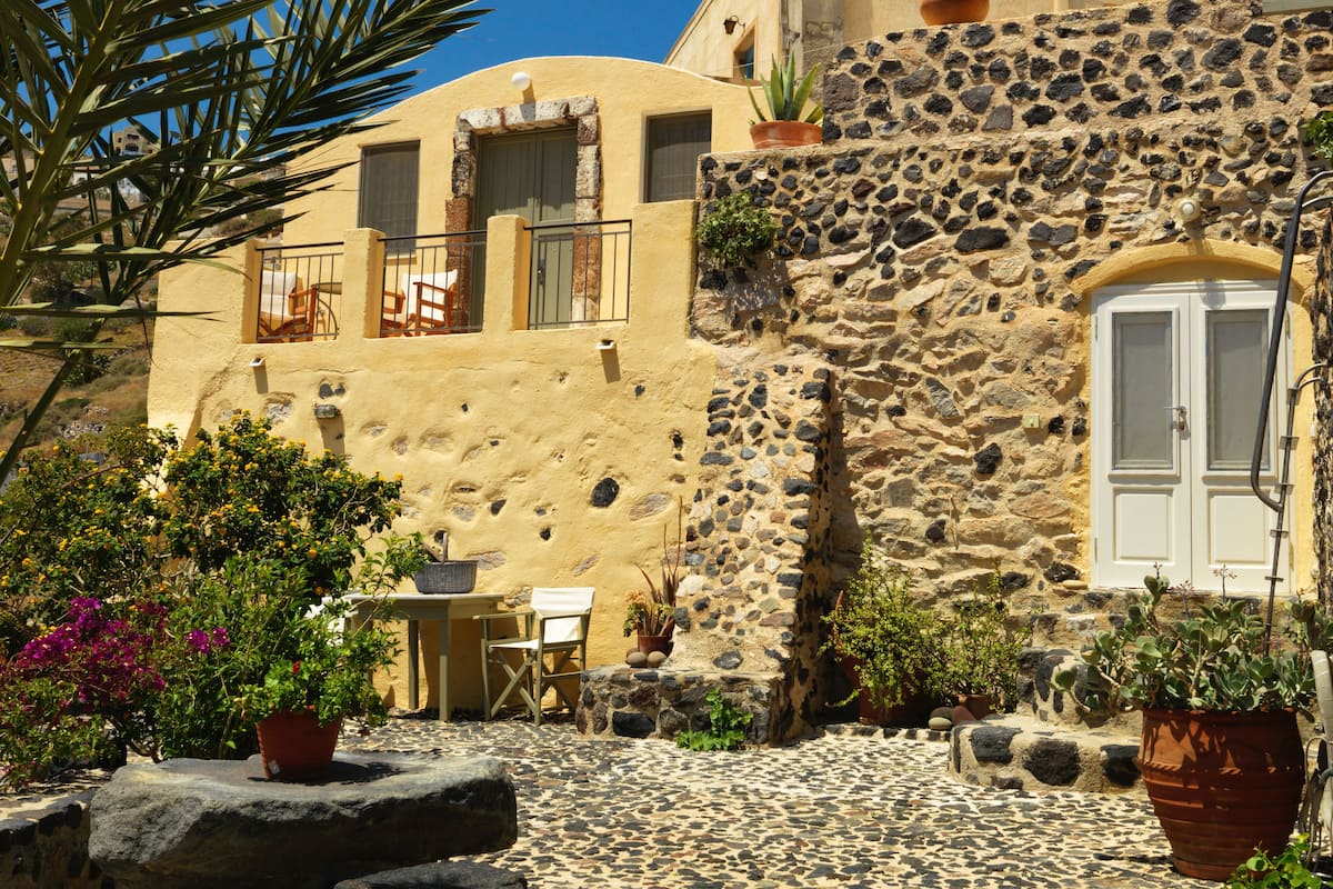A stone building with a white door, a small table with a chair, and potted plants.