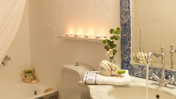 A bathroom with a bathtub, a sink, and a mirror. There are candles on a shelf above the bathtub, and a plant next to the mirror.