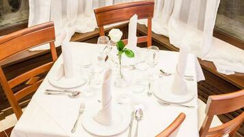 Una mesa redonda de comedor con mantel blanco, servida con platos, copas y velas.