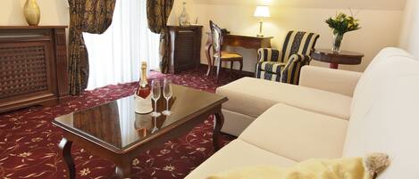 A hotel room with a sofa, armchair, and a small table with a bottle and glasses.