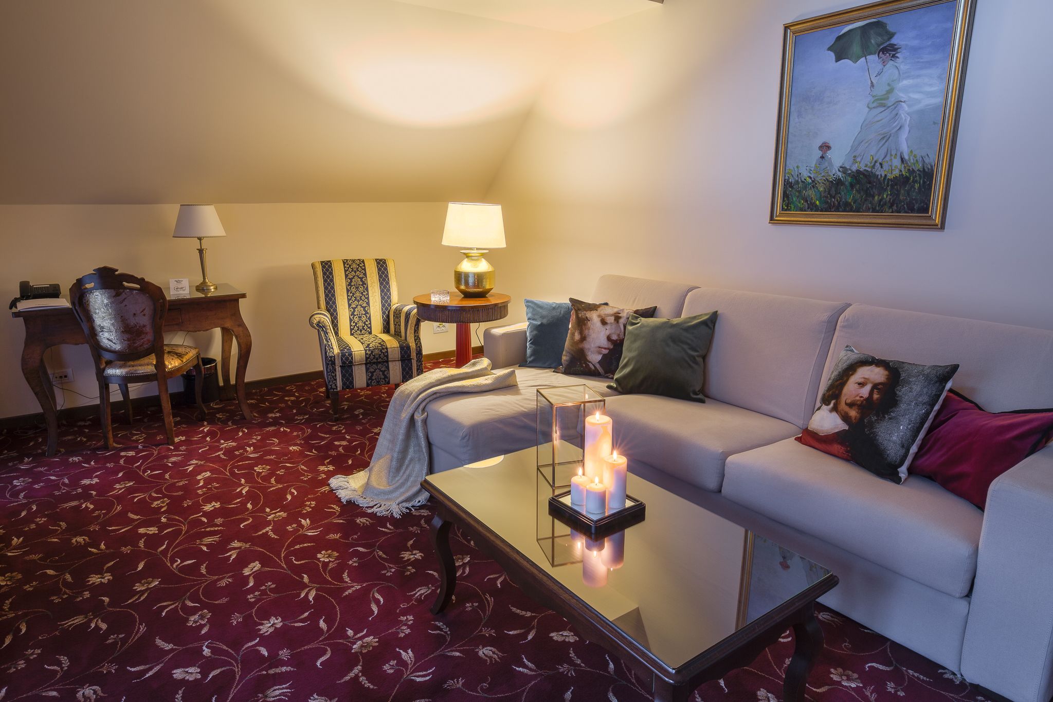 Una sala de estar acogedora con un sofá, dos sillones, una mesita de centro con velas, una lámpara y un cuadro en la pared.