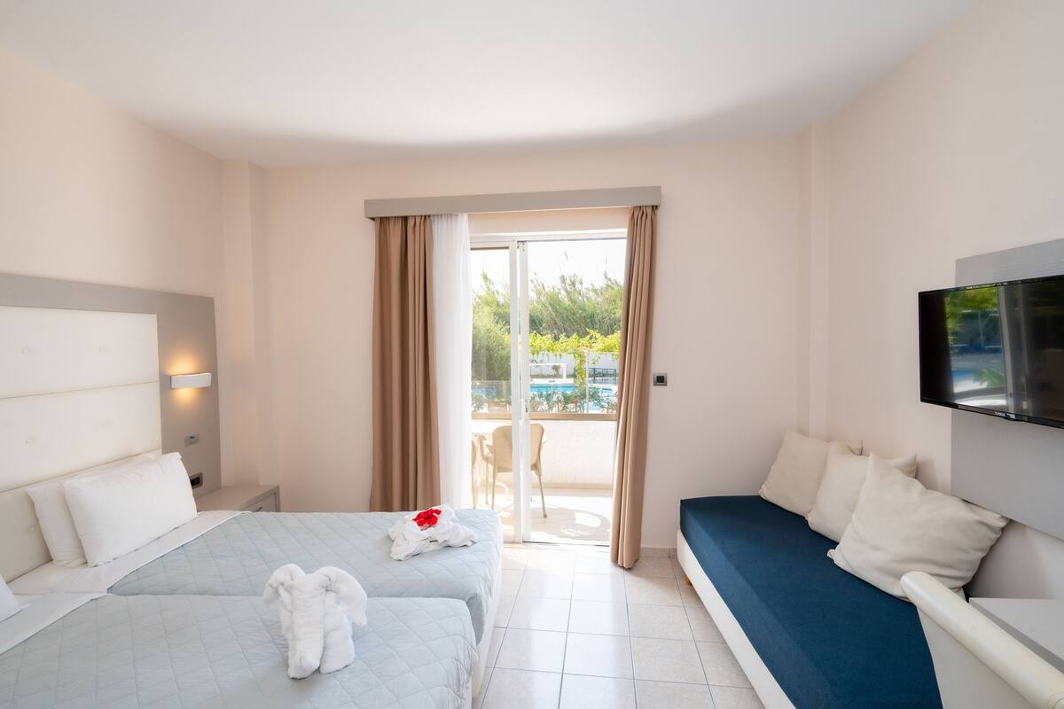 Habitación de hotel con dos camas, televisión, balcón y vista a la piscina, además de una puerta corrediza de cristal.