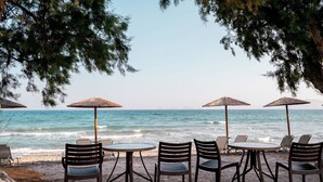 Un café situé en bord de mer, avec des tables et des chaises placées sous des parasols, offrant une vue sur l’océan.