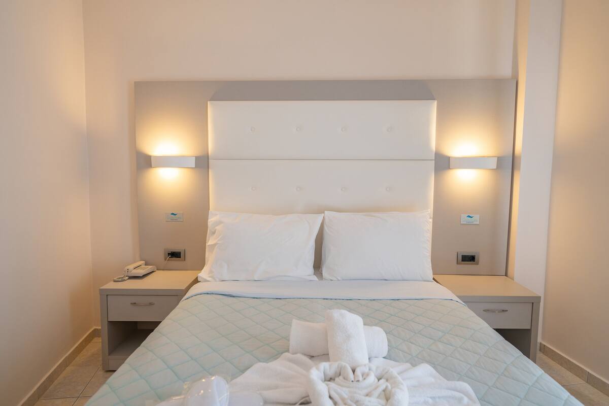 Una habitación de hotel con una cama, dos mesitas de noche y dos luces fijadas a la pared.