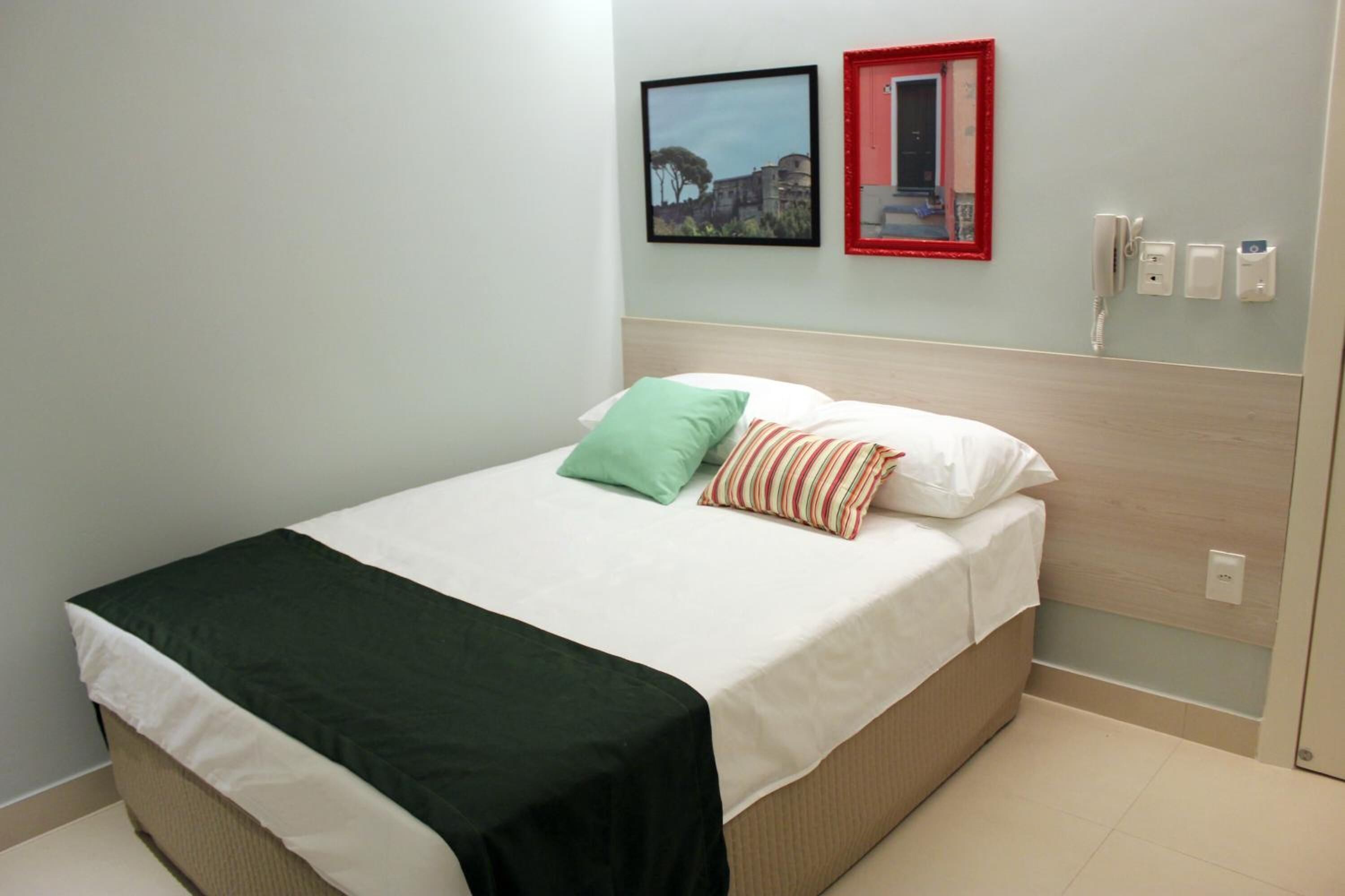 A neatly made bed with a green and striped pillow, a white bedspread, and a dark green throw.