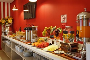 Un bufé con diversas frutas y bebidas, una máquina de café y un cartel de prohibido fumar en la pared.