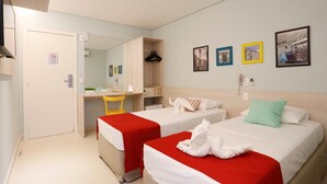 A hotel room with two beds, a desk, and a chair. There are framed pictures on the wall and a no-smoking sign on the door. - Portofino Hotel (Teresina)