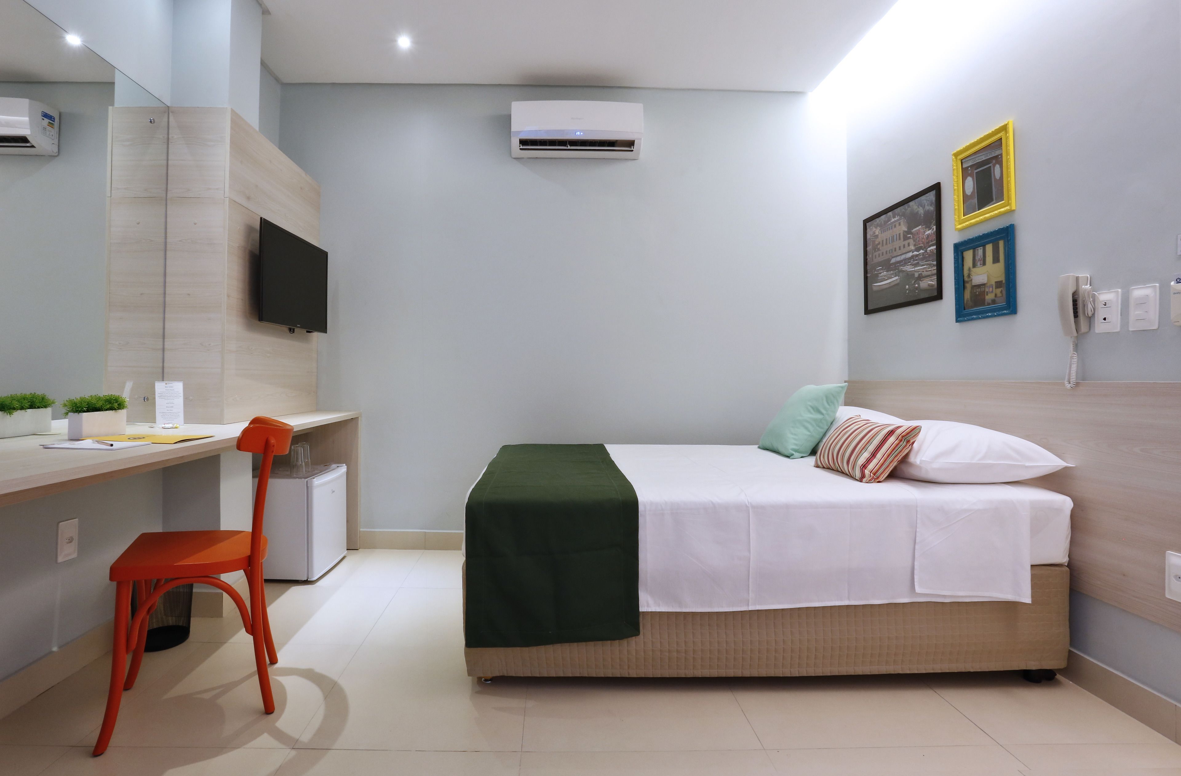 Una habitación de hotel moderna con una cama, un escritorio con silla, un televisor, aire acondicionado y un teléfono.