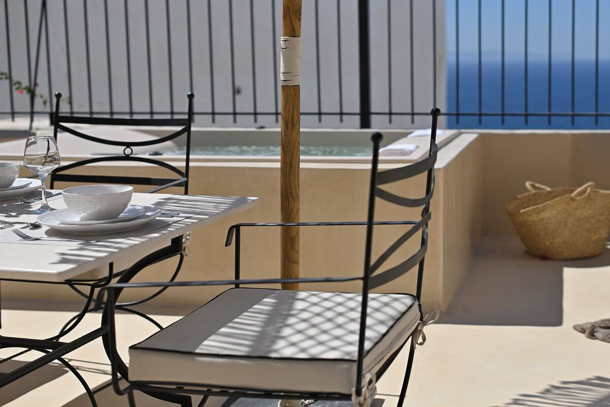 Un área de comedor al aire libre con una mesa para dos, sillas y vista al océano.