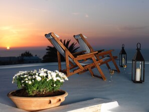 A sunset view with two wooden chairs and a potted plant on a terrace. - OIA Unique Homes by K&K (Santorini)