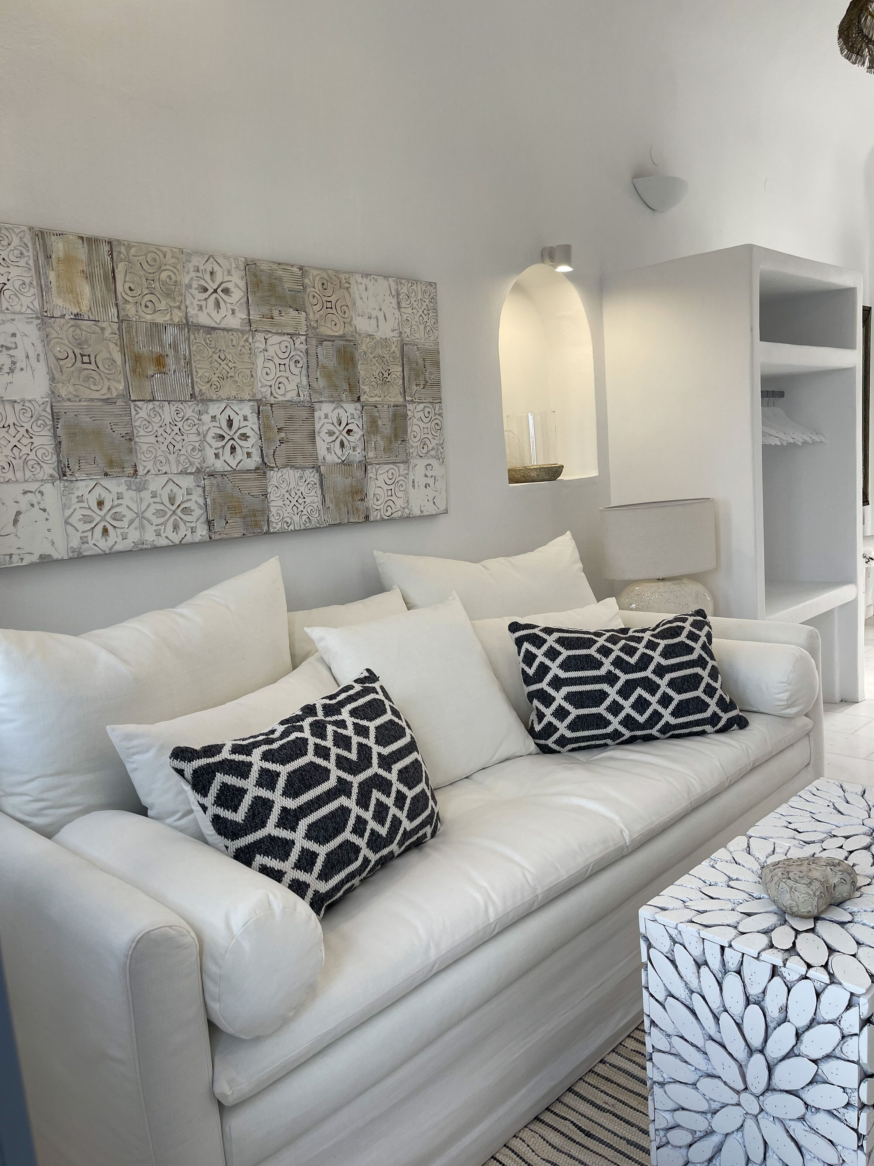 A modern living room with a white leather sofa, patterned cushions, a decorative wall, and a white side table.