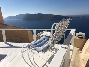 Een witte metalen stoel met kussen op een balkon met uitzicht op water en kliffen.