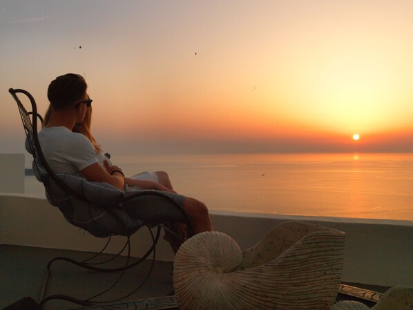 A person sitting on a chair overlooking a sunset over the water. - OIA Unique Homes by K&K (Santorini)