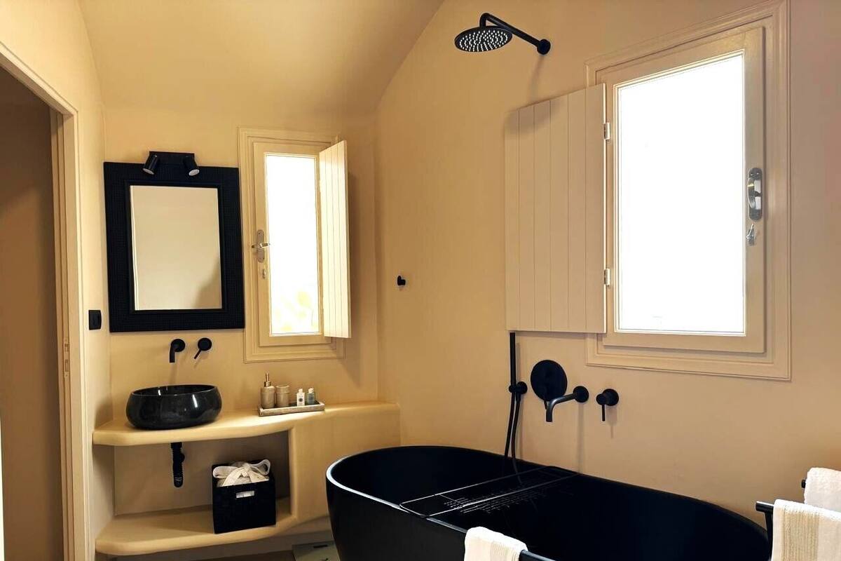 Un baño con una bañera negra, un lavamanos con espejo y una ventana que proporciona luz natural.