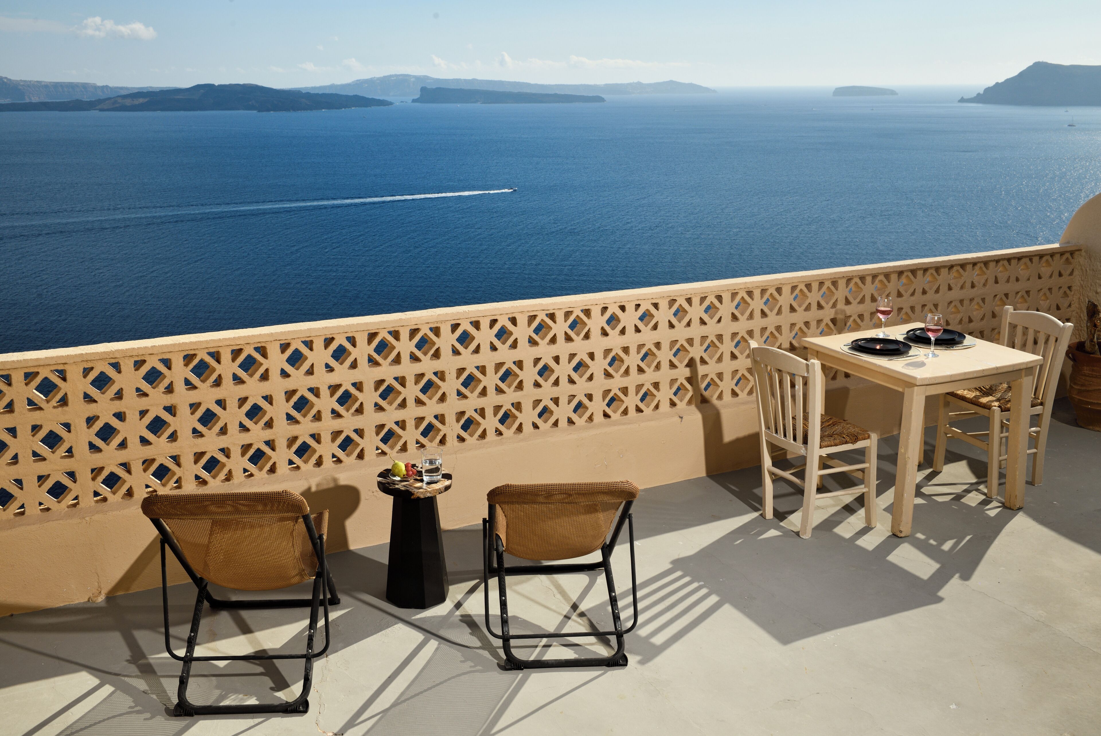 A terrace with a table and chairs overlooking the sea, with a view of distant islands.