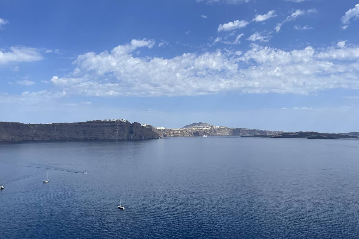 Un mar tranquilo con un velero y una pequeña isla con acantilados a lo lejos.