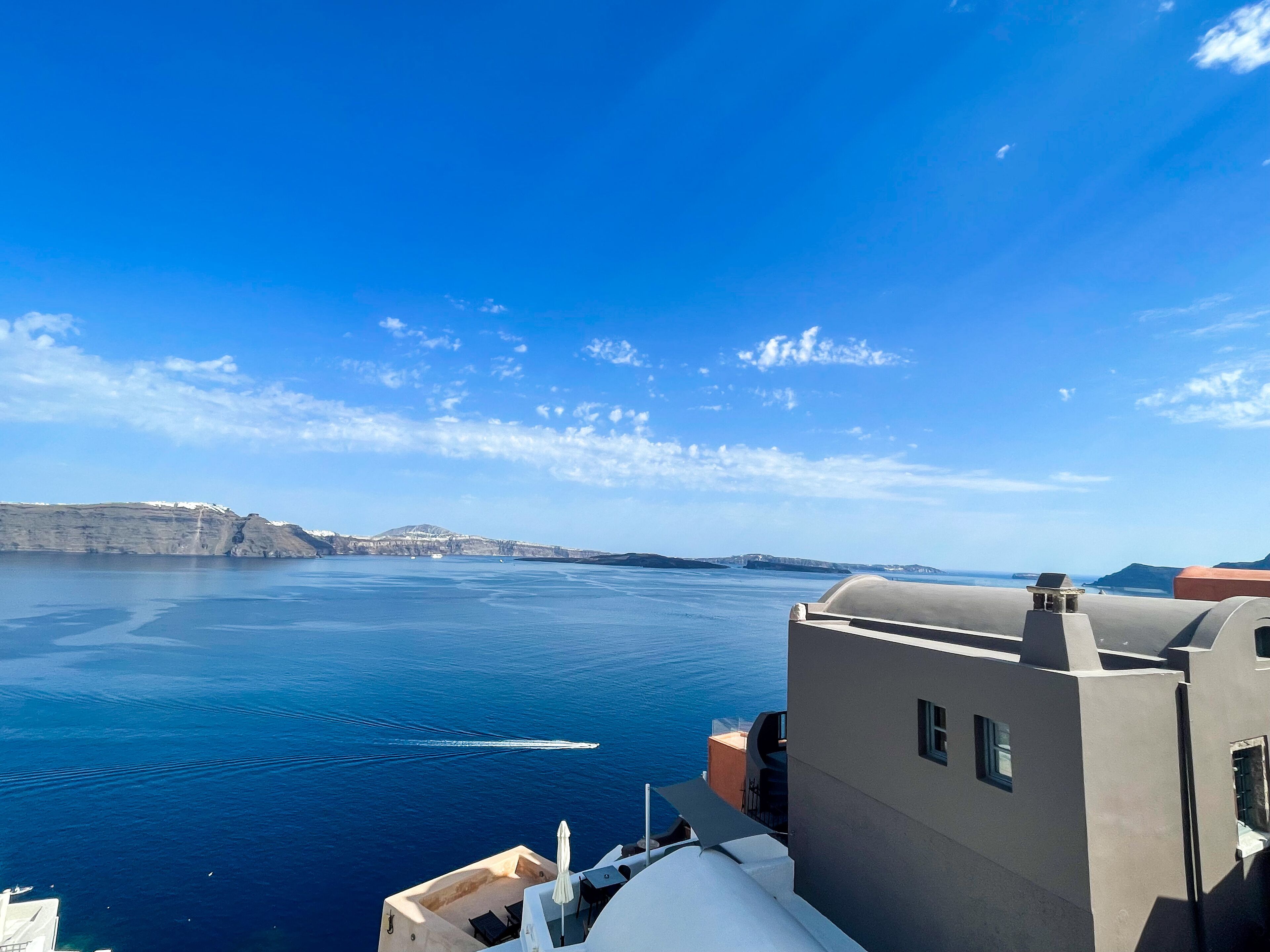 Vista costera con cielo despejado, un barco en el agua y edificios de estilo arquitectónico moderno.