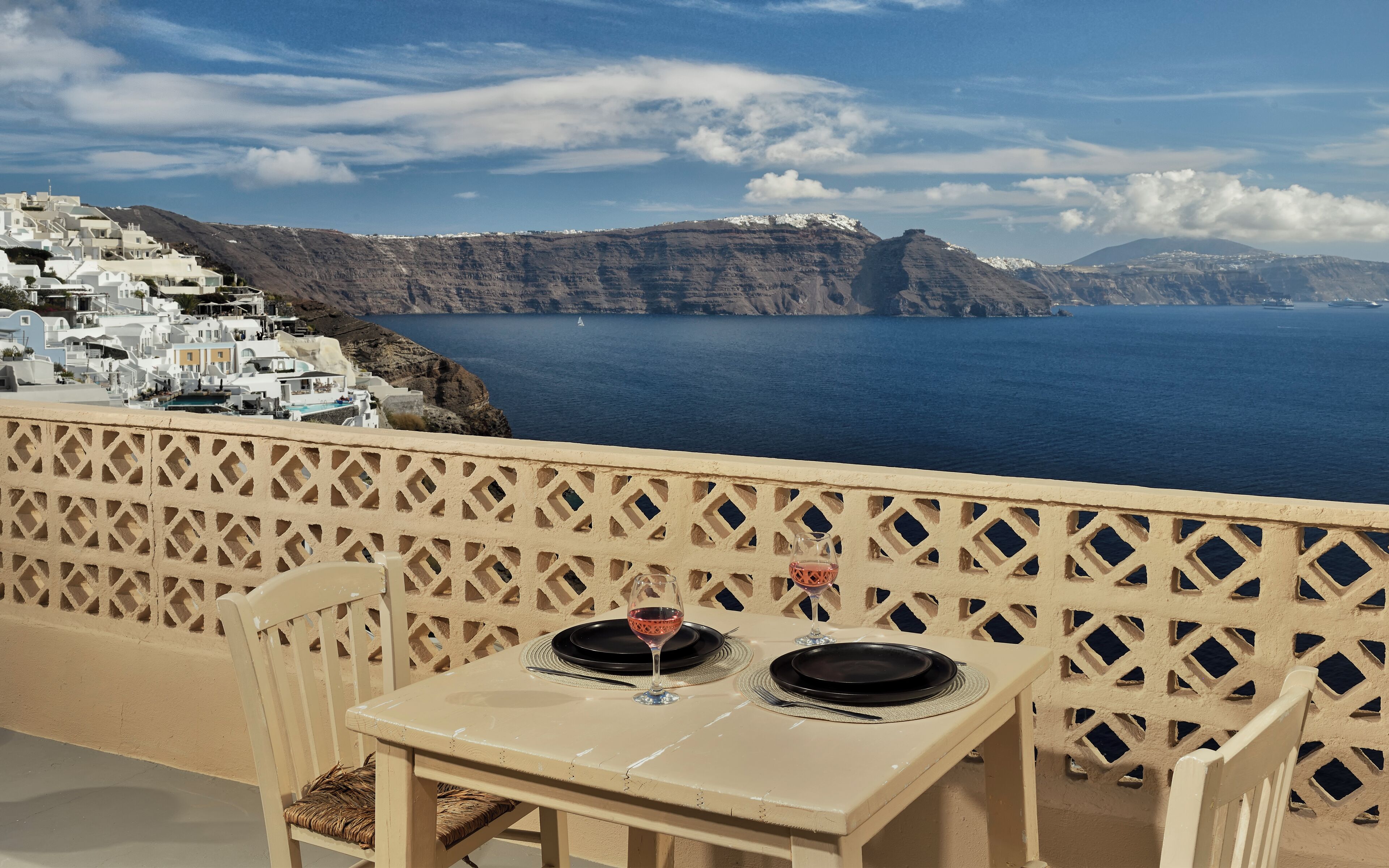 A table with two plates and a glass of red wine, set against a scenic backdrop of a coastal village and the sea.