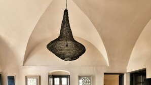 A spacious living room with a high arched ceiling, a hanging light fixture, a sofa with cushions, a coffee table, and a rug. - OIA Unique Homes by K&K (Santorini)