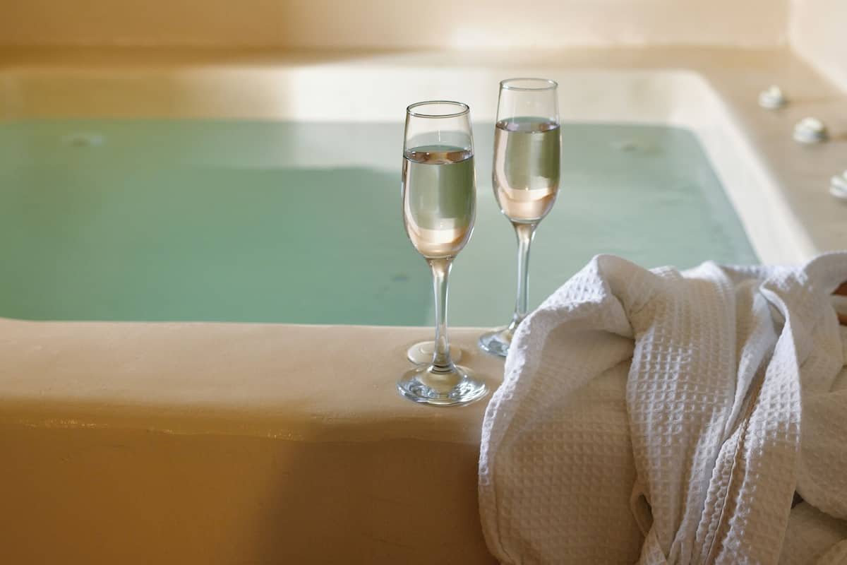 Una bañera con dos vasos de agua, una toalla y una bata.