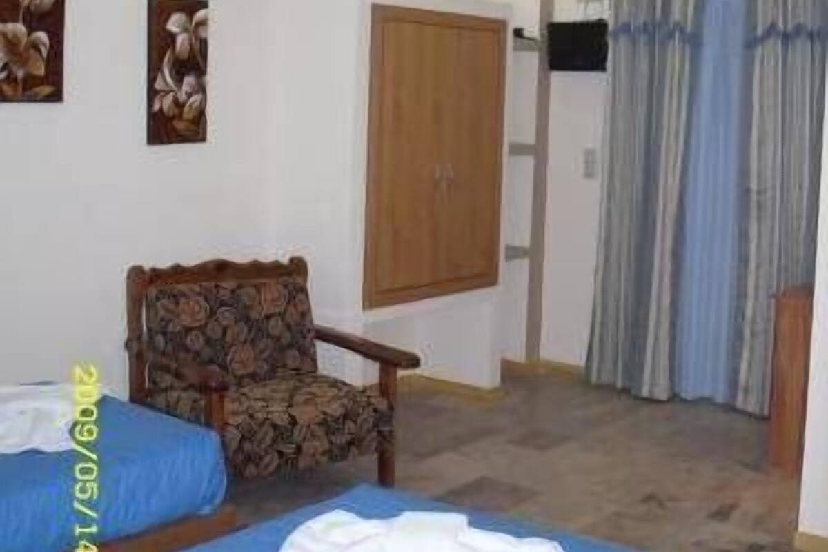Un dormitorio con dos camas, un armario de madera, una silla y una ventana con cortinas.
