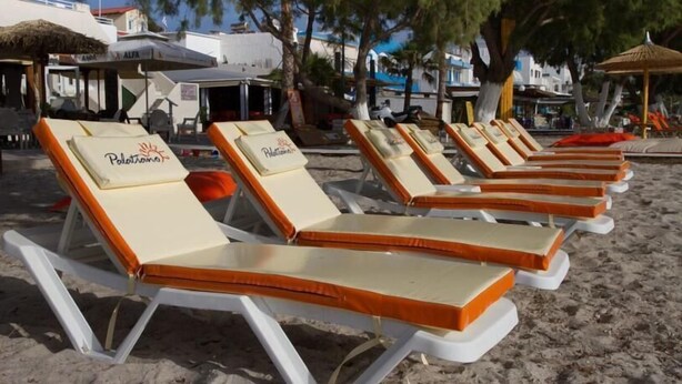 De nombreuses chaises longues avec des coussins sont alignées sur une plage de sable, certaines portant la marque « Polo », sous un ciel dégagé.
