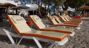 Filas de tumbonas con cojines en una playa de arena, algunas con la marca 'Polo', bajo un cielo despejado.