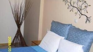 Une chambre à coucher avec un lit, des oreillers, une décoration murale représentant un arbre et un vase.