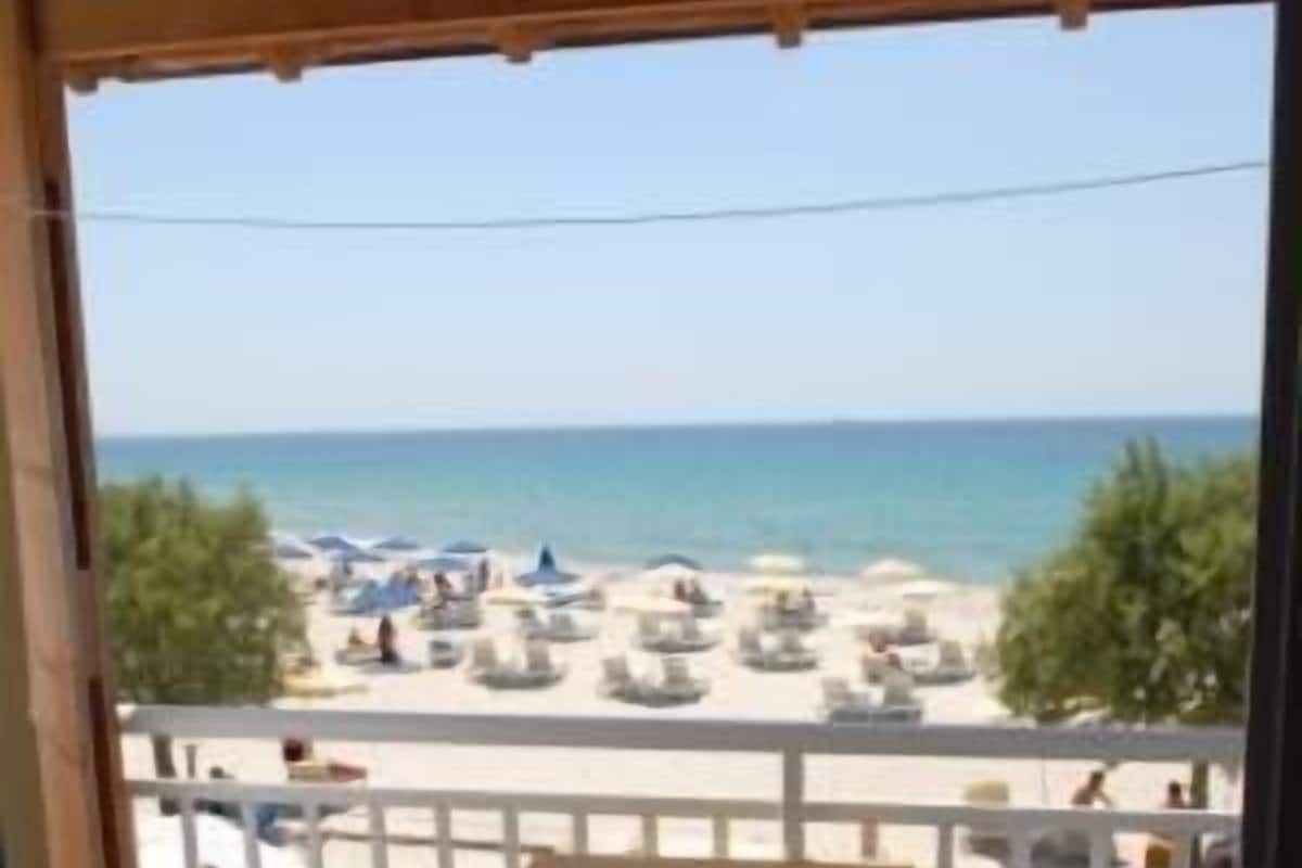 Balcón con mesa y sillas con vista a una playa con sombrillas y gente.