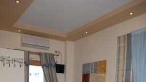 Une pièce avec un canapé marron, un lit bleu, un tableau accroché au mur et une vue sur la mer par la fenêtre.