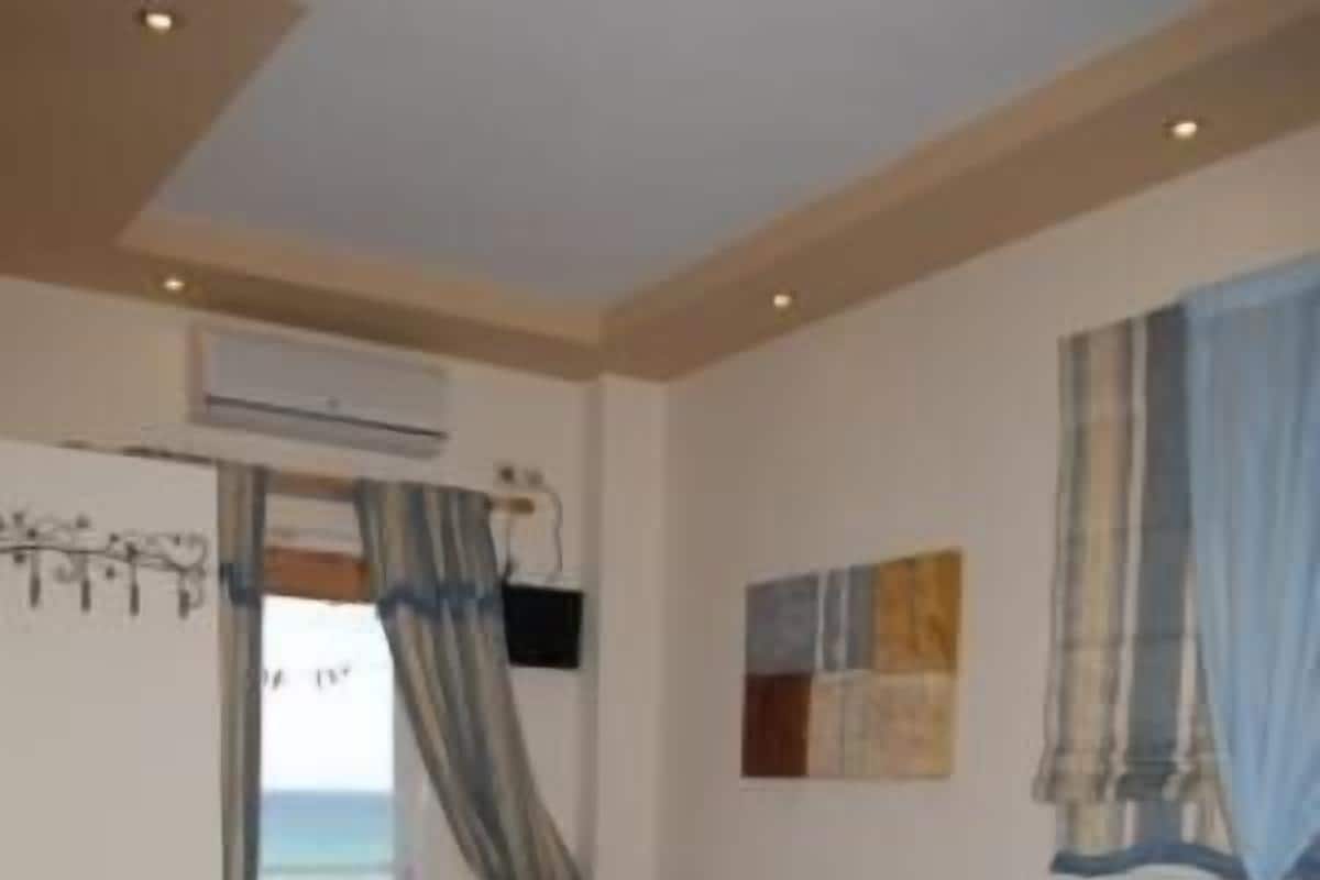 Una habitación con un sofá marrón, una cama azul, un cuadro en la pared y vista al mar por una ventana.