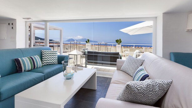 Una sala moderna con sofá, mesa de centro y vistas a la playa y las montañas.