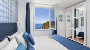Un dormitorio con cama, laptop, ventana con vista al mar y armario.