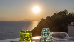 Una mesa con vasos y vista al mar al atardecer.