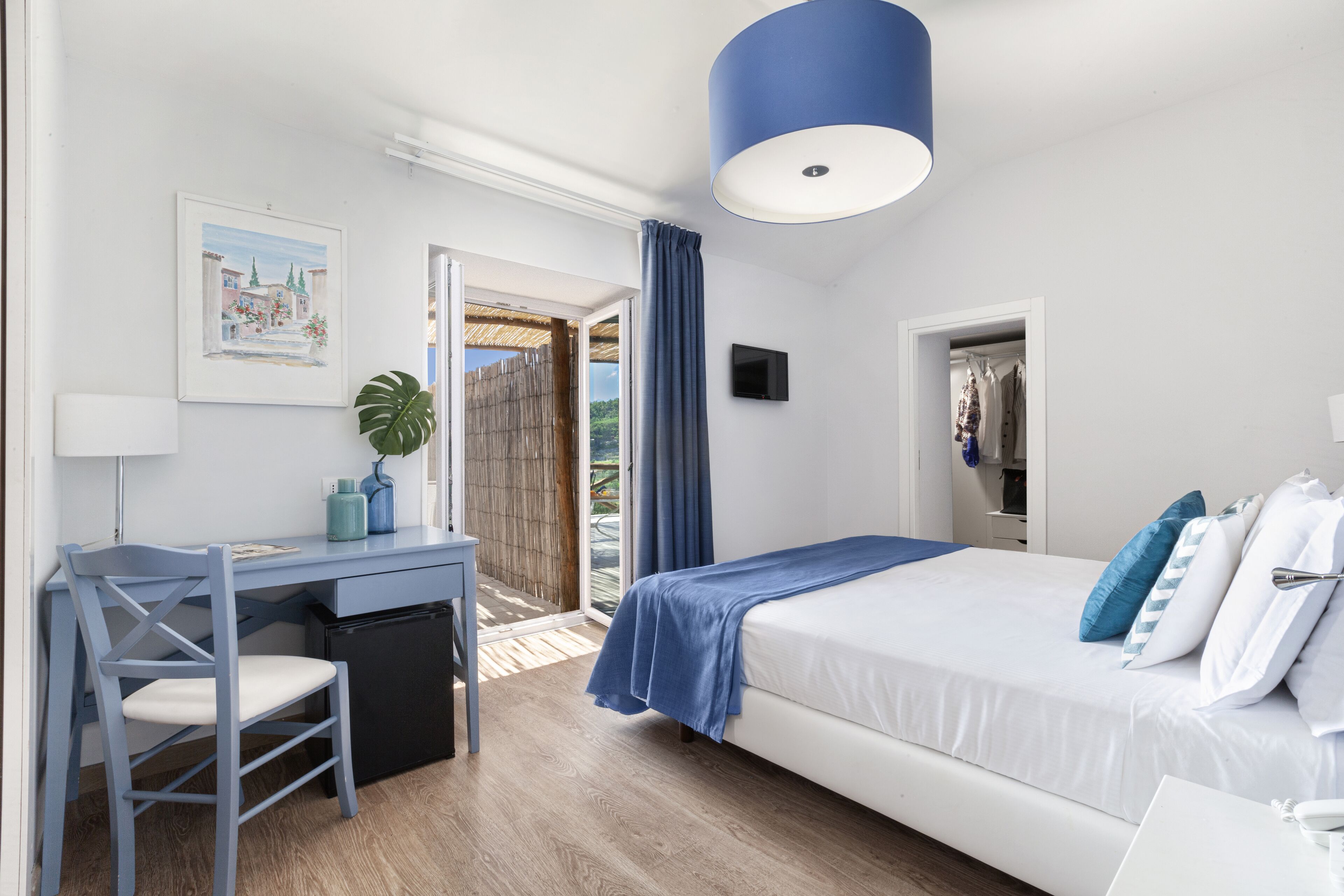Une chambre à coucher comprenant un lit, un bureau, une chaise, un téléviseur et une fenêtre donnant sur un paysage verdoyant.