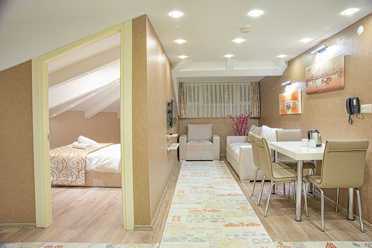 A hotel room with a bed, a desk, a chair, a small sofa, a dining table, and a telephone.