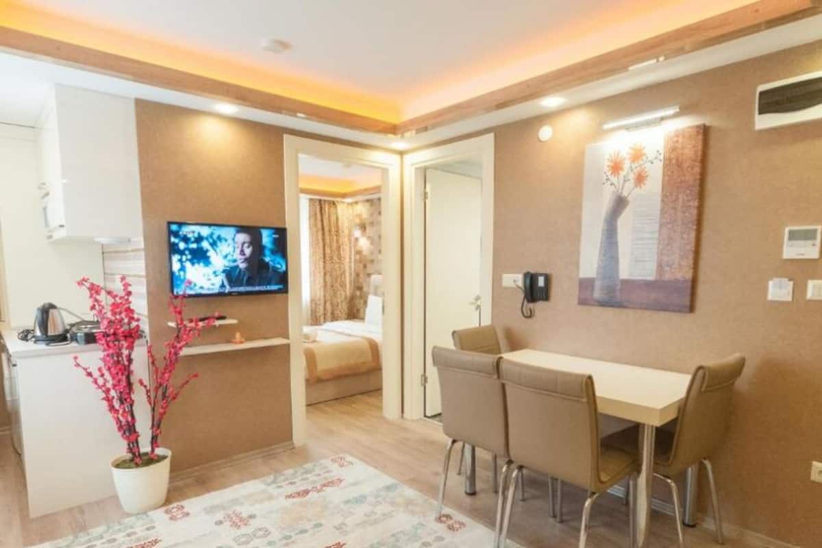 A modern hotel room with a dining area, a TV, a potted plant, and a painting on the wall.
