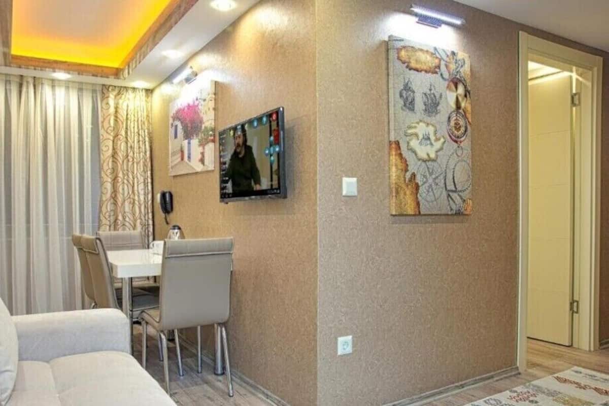 A modern living room with a sofa, a dining table with chairs, and a TV mounted on the wall.